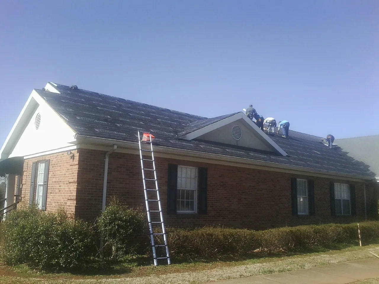 Crew tearing shingles off a brick ranch roof with a ladder set — Emergency Roof Repair work by our crew in Brunswick